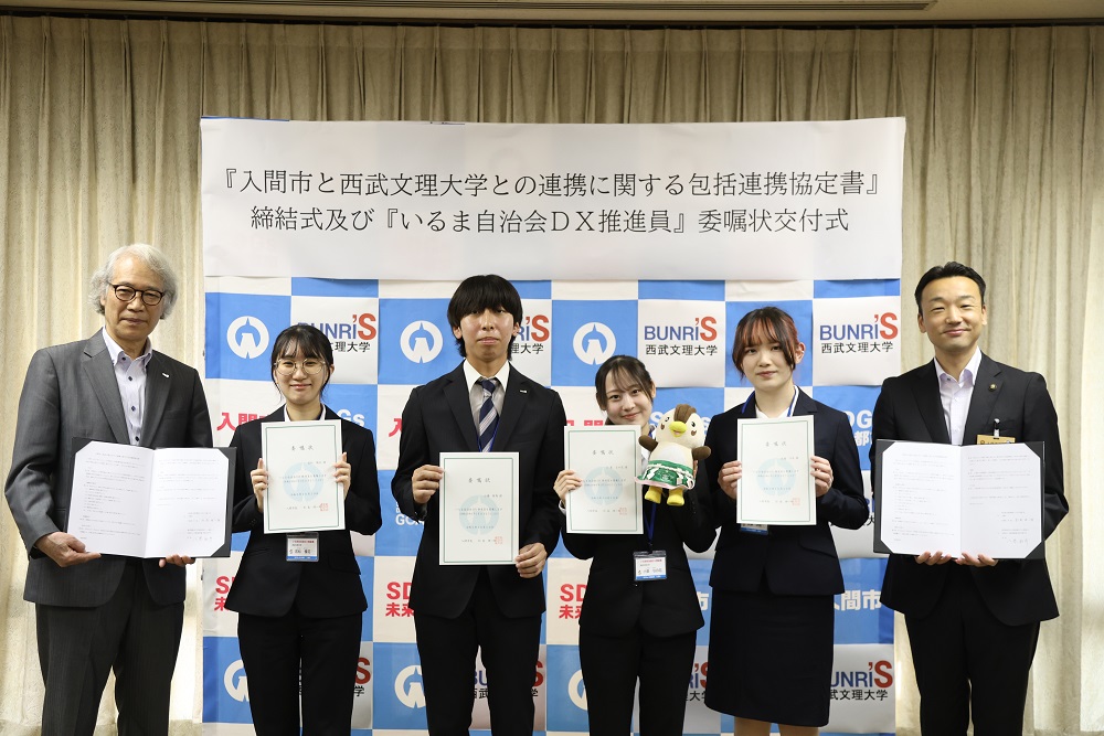 写真左から八巻和彦学長、サービス経営学部の学生3名、看護学部の学生1名、杉島理一郎入間市長